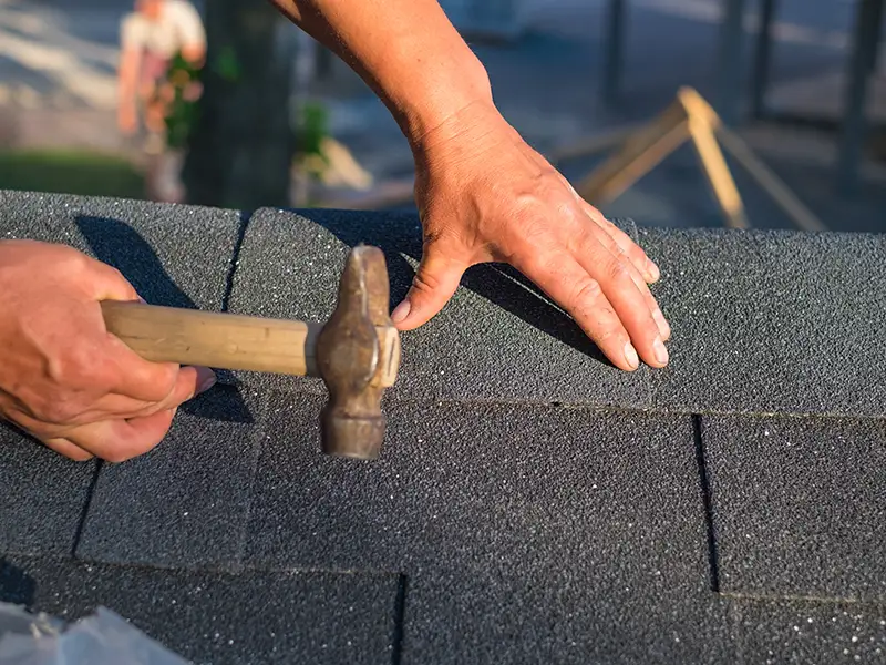 Roofer installing new shingles with a hammer